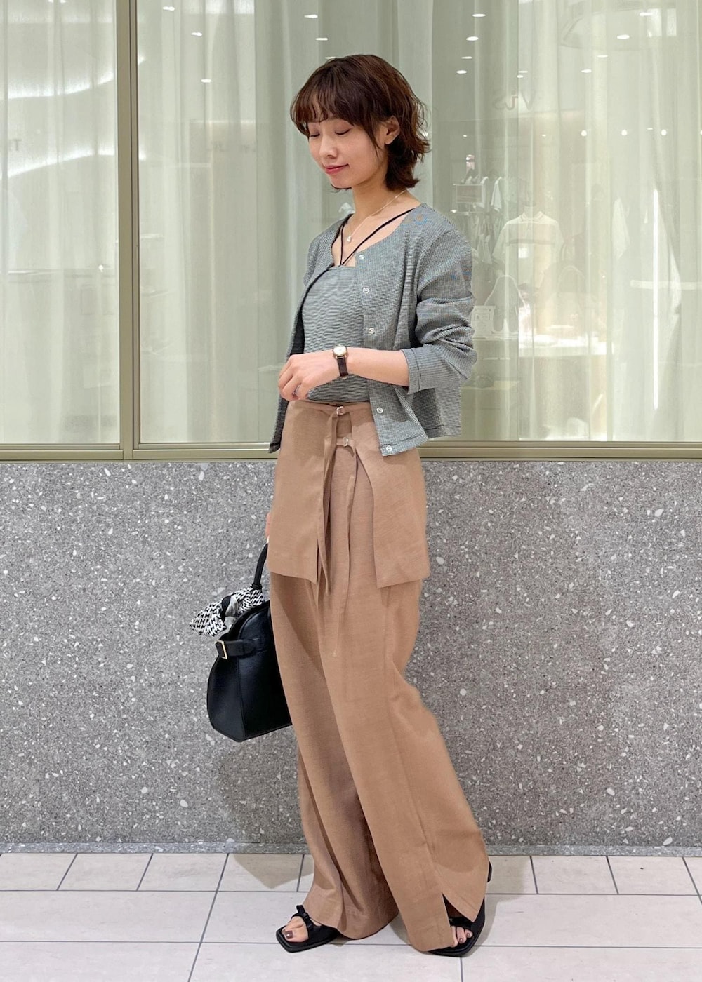 ブラック系のサンダル、ブラウン系のスラックス、ブラック系のトートバッグを着用したレディースの夏コーディネートの2枚目の写真