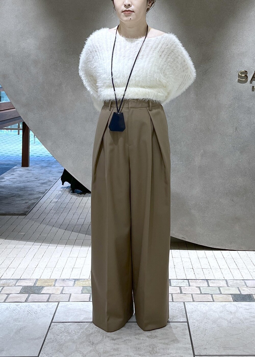 ベージュ系のスラックス、ベージュ系のチェスターコート、ホワイト系のニット/セーターを着用したレディースの秋コーディネートの9枚目の写真