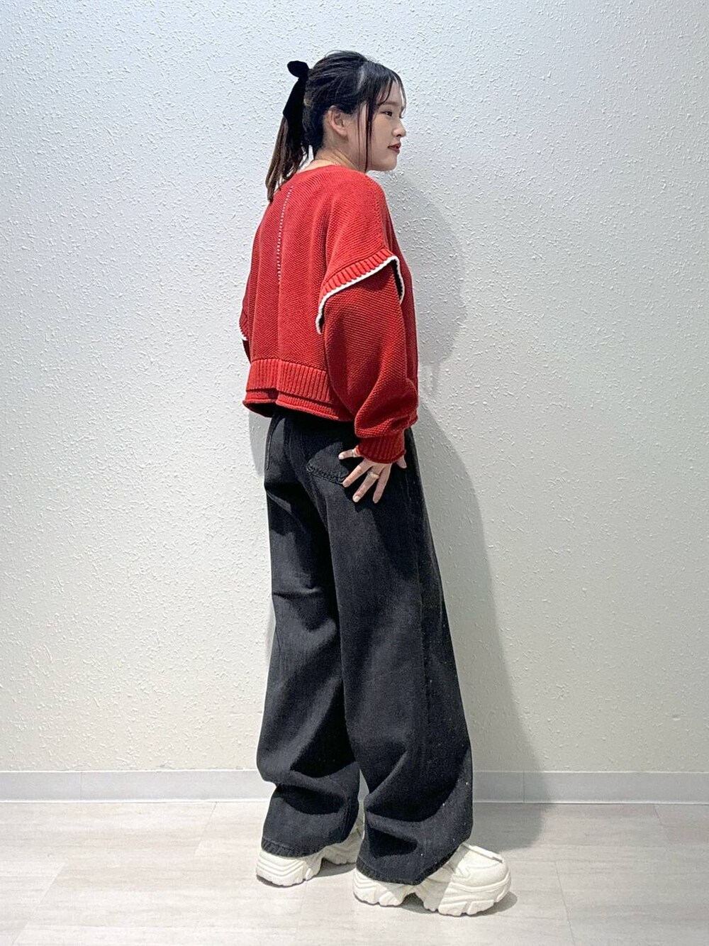 レッド系のニット/セーター、ホワイト系のスニーカー、ブラック系のデニムパンツを着用したレディースの秋コーディネートの3枚目の写真