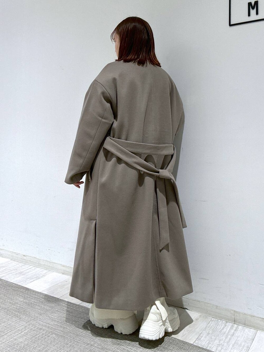 ホワイト系のスカート、ブラウン系のトレンチコート、グリーン系のニット/セーターを着用したレディースの冬コーディネートの2枚目の写真