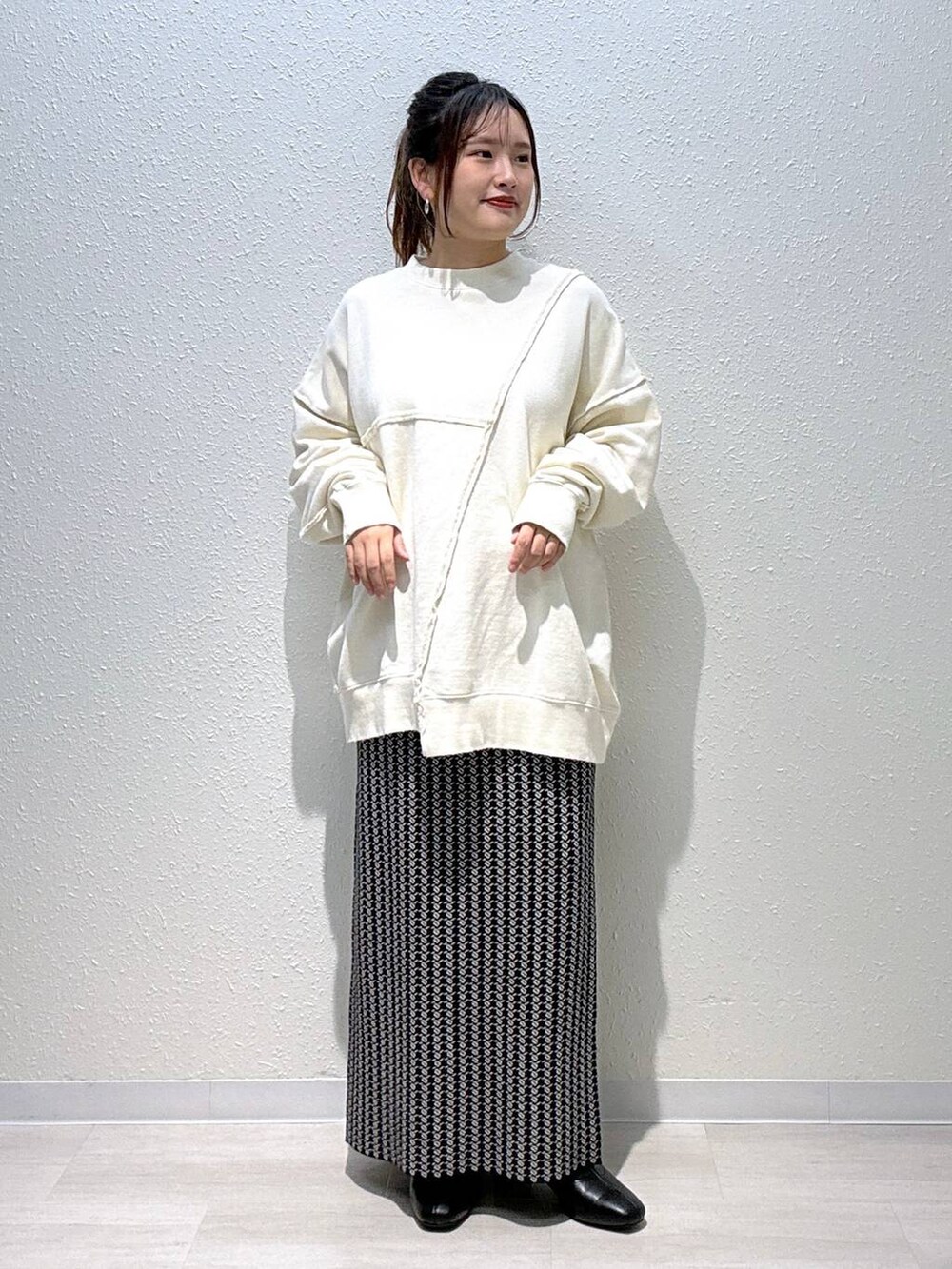 ブラック系のスカート、ホワイト系のスウェット、ブラック系のブーツを着用したレディースの秋コーディネートの2枚目の写真