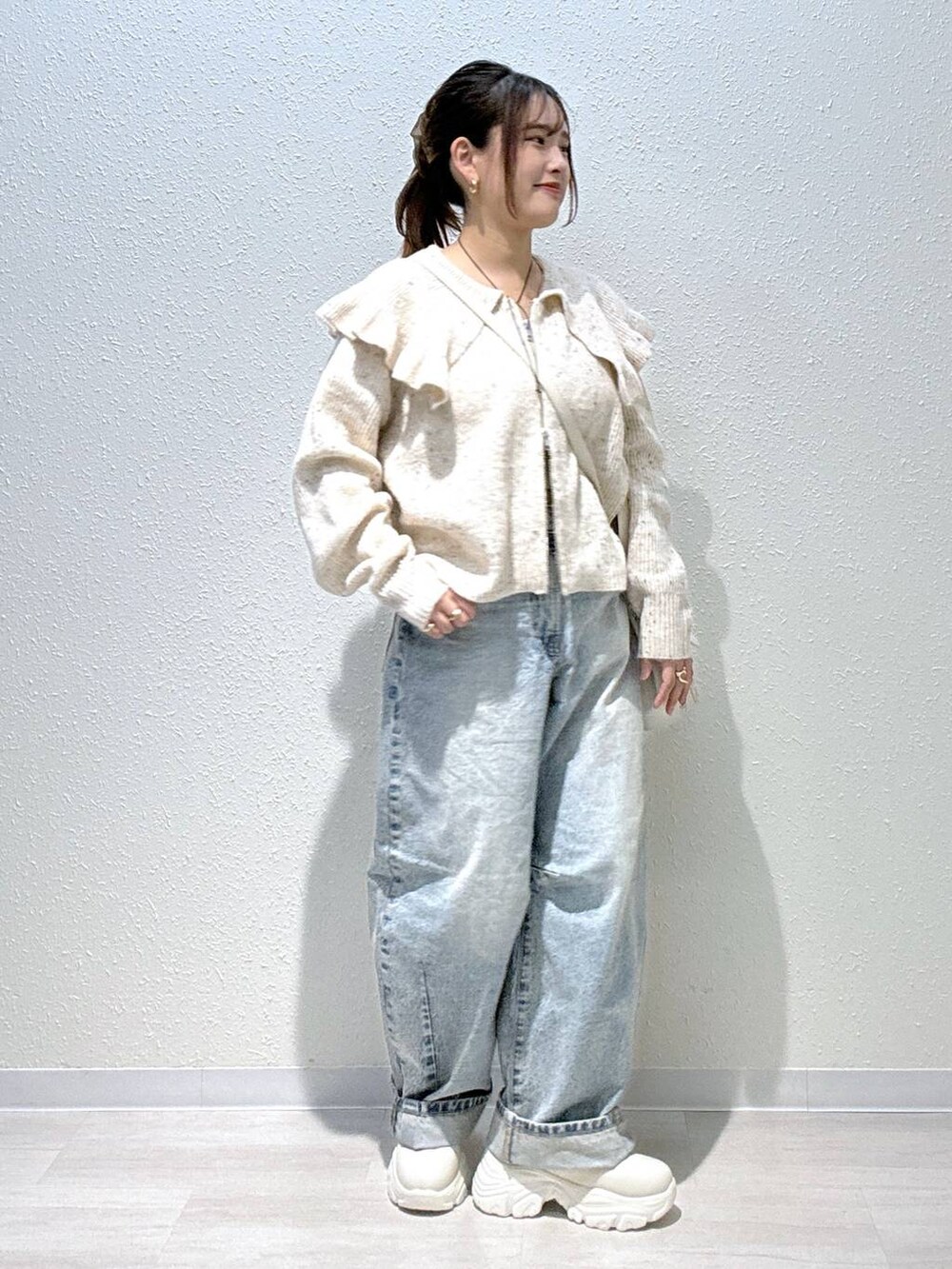 ブルー系のデニムパンツ、ホワイト系のショルダーバッグ、ホワイト系のブーツを着用したレディースの秋コーディネートの2枚目の写真