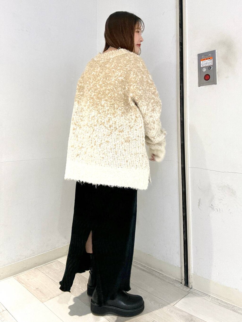 ブラック系のブーツ、ホワイト系のニット/セーター、ブラック系のスカートを着用したレディースの冬コーディネートの2枚目の写真