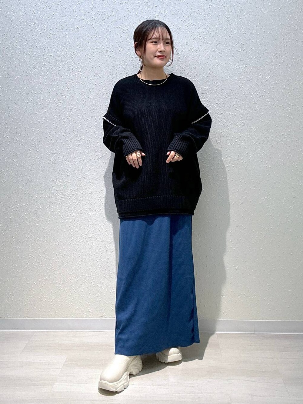 ブルー系のスカート、ブラック系のニット/セーター、ホワイト系のブーツを着用したレディースの秋コーディネートの2枚目の写真