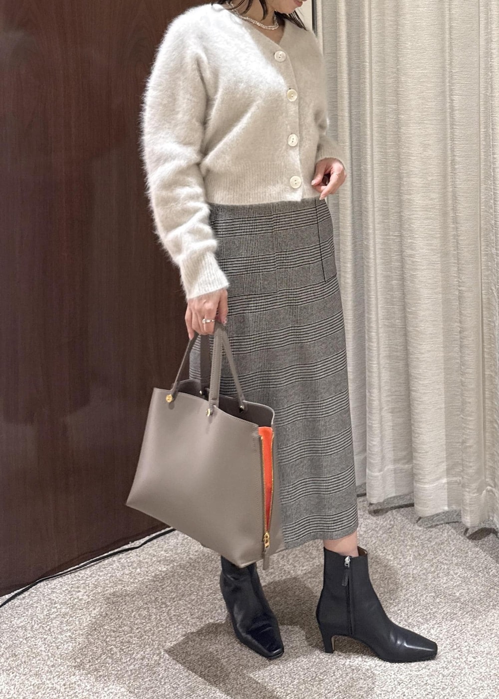 ブラウン系のトートバッグ、ブラック系のブーツ、ブラック系のスカートを着用したレディースの冬コーディネートの3枚目の写真