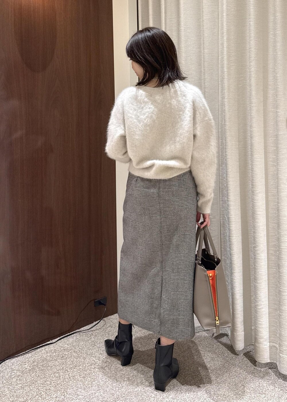 ブラウン系のトートバッグ、ブラック系のブーツ、ブラック系のスカートを着用したレディースの冬コーディネートの2枚目の写真