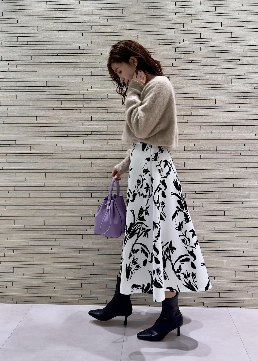 パープル系のハンドバッグ、ブラック系のブーツ、ベージュ系のニット/セーターを着用したレディースの秋コーディネートの2枚目の写真