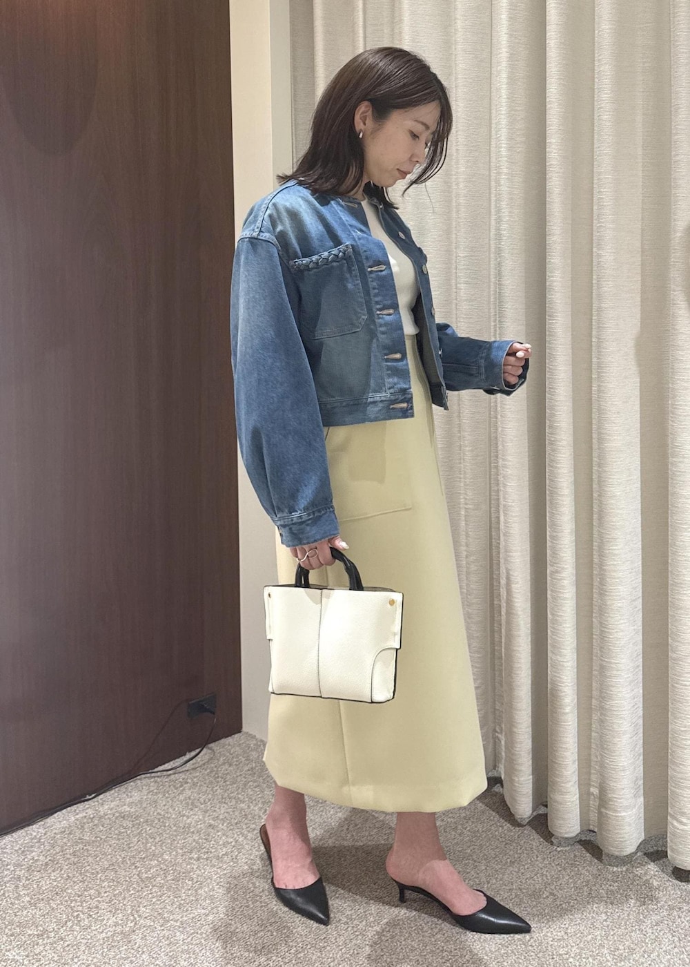 ホワイト系のハンドバッグ、ベージュ系のスカート、ブルー系のデニムジャケットを着用したレディースの春コーディネートの2枚目の写真