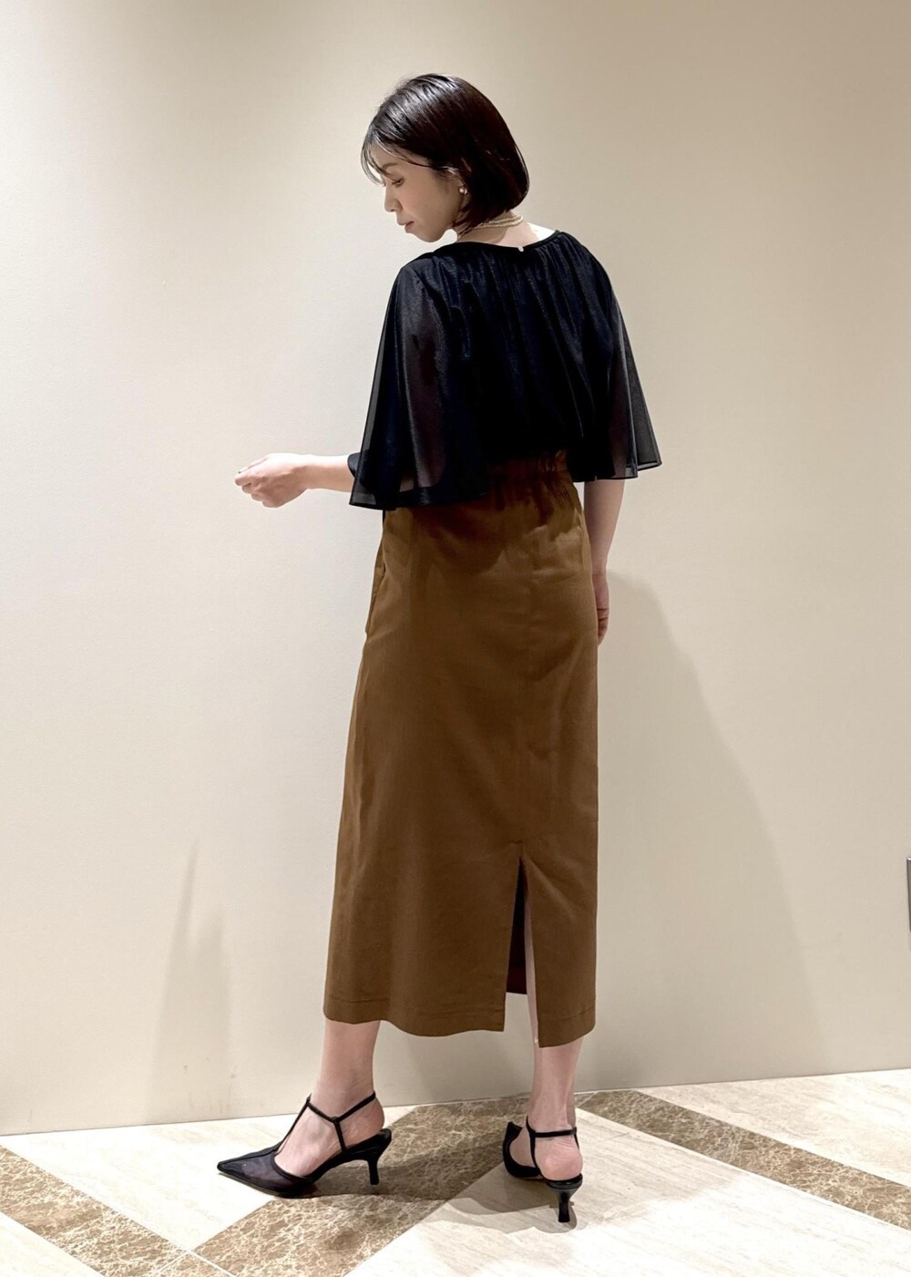 ホワイト系のショルダーバッグ、ブラック系のパンプス、ブラウン系のスカートを着用したレディースの春コーディネートの3枚目の写真