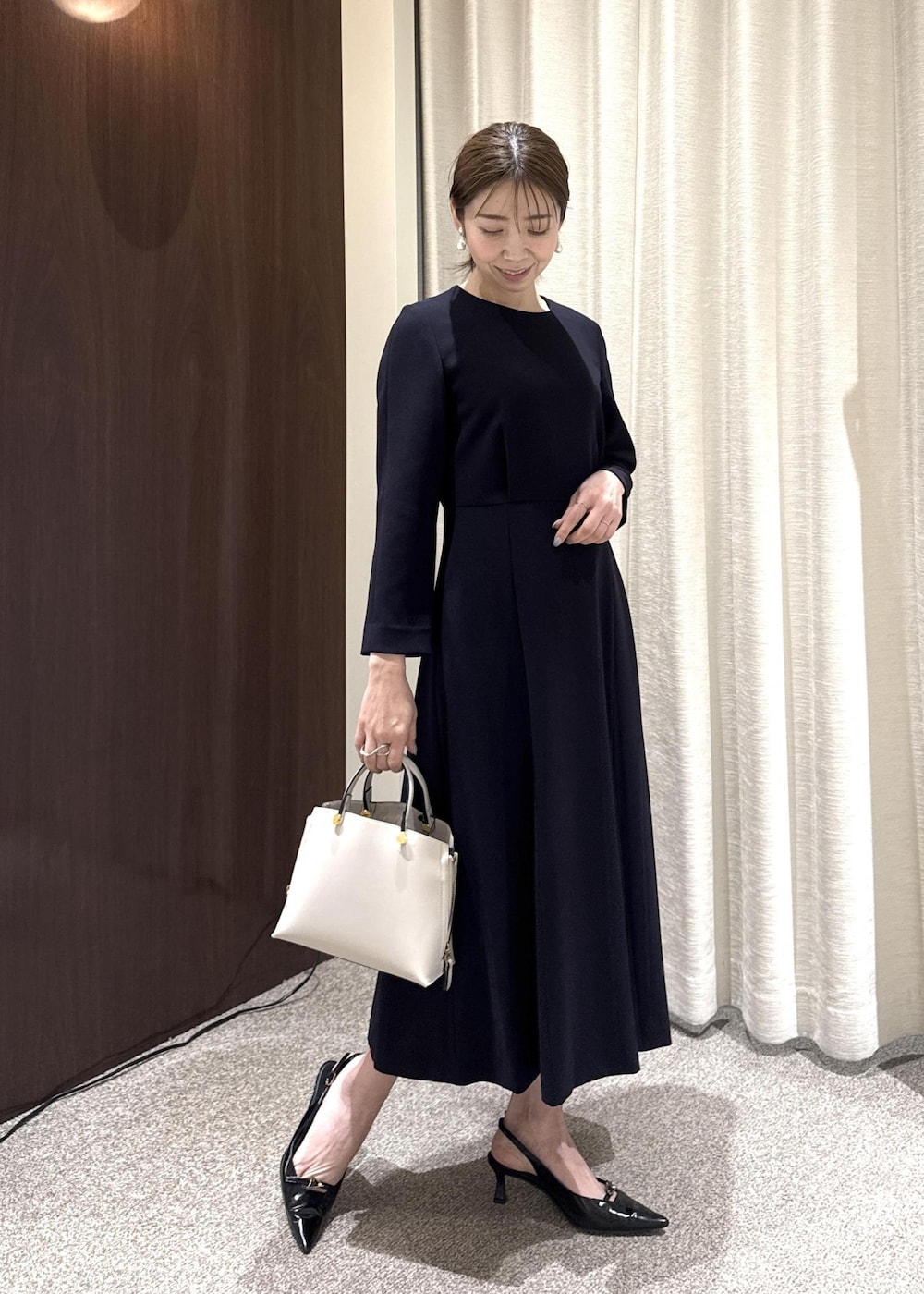 グレー系のハンドバッグ、ブルー系のワンピース、ブラック系のノーカラージャケットを着用したレディースの冬コーディネートの4枚目の写真