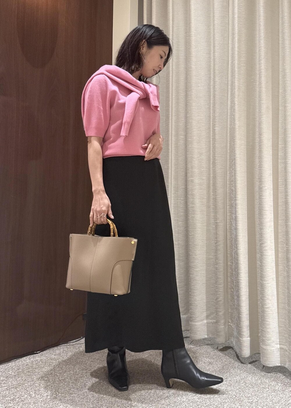 ブラック系のスカート、ベージュ系のハンドバッグ、ブラック系のブーツを着用したレディースの秋コーディネートの2枚目の写真
