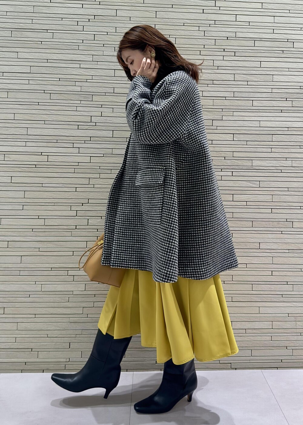 ブラック系のブーツ、ブラック系のその他アウター、イエロー系のハンドバッグを着用したレディースの冬コーディネートの2枚目の写真