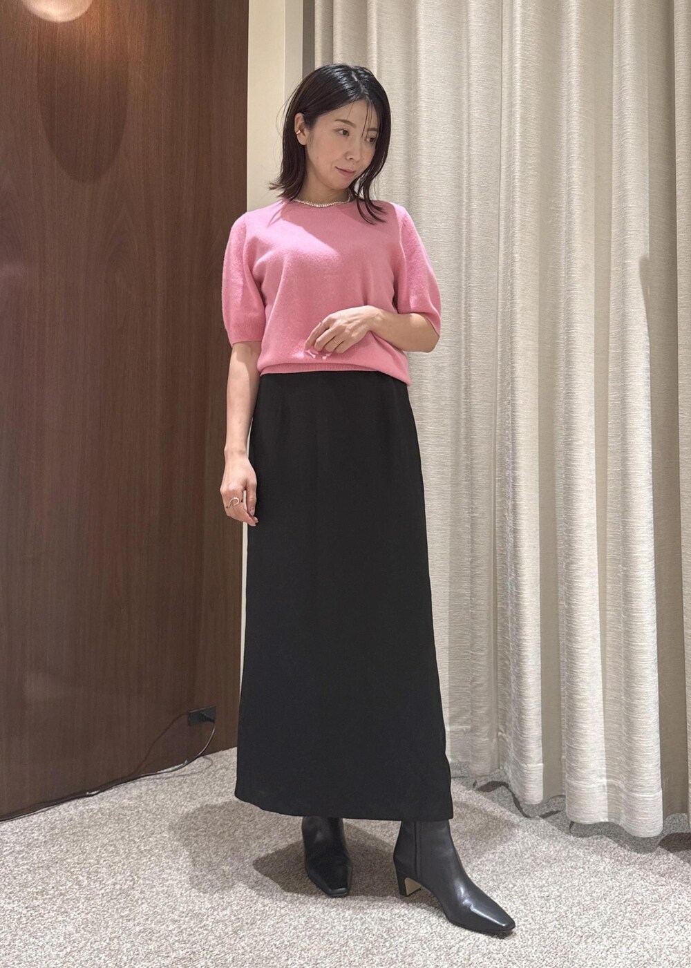 ブラック系のスカート、ベージュ系のハンドバッグ、ブラック系のブーツを着用したレディースの秋コーディネートの4枚目の写真