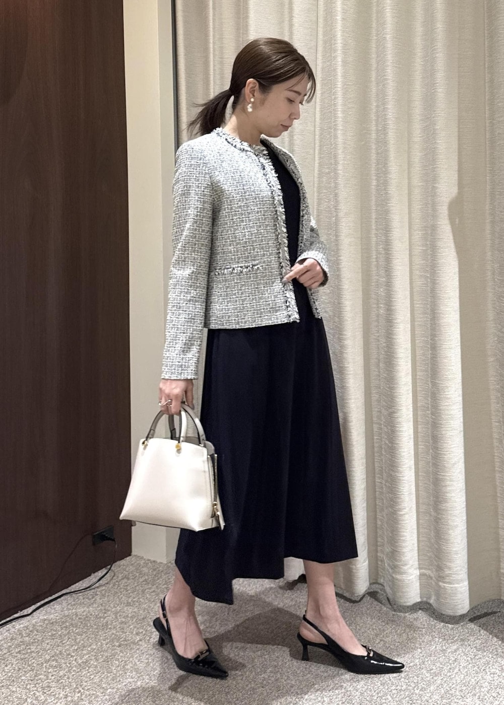 グレー系のハンドバッグ、ブルー系のワンピース、ブラック系のノーカラージャケットを着用したレディースの冬コーディネートの2枚目の写真