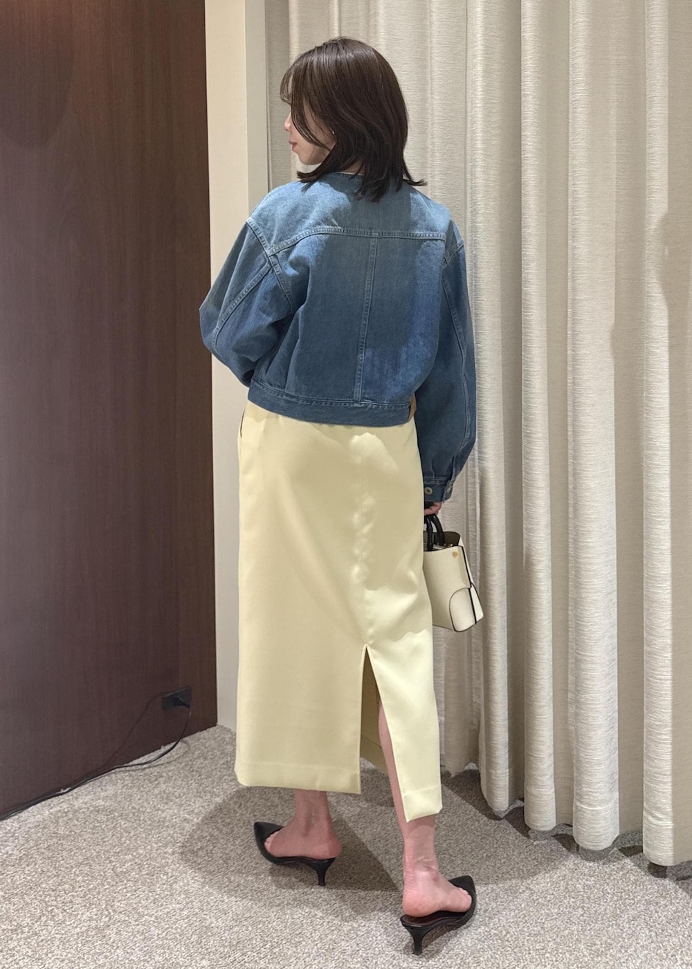 ホワイト系のハンドバッグ、ベージュ系のスカート、ブルー系のデニムジャケットを着用したレディースの春コーディネートの3枚目の写真