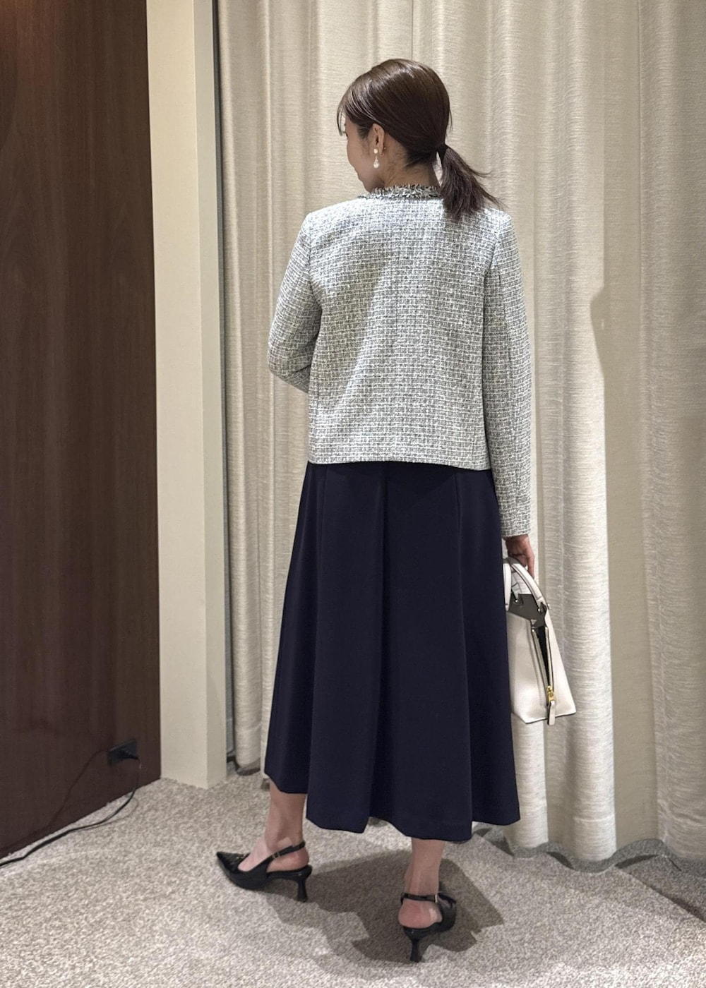 グレー系のハンドバッグ、ブルー系のワンピース、ブラック系のノーカラージャケットを着用したレディースの冬コーディネートの3枚目の写真