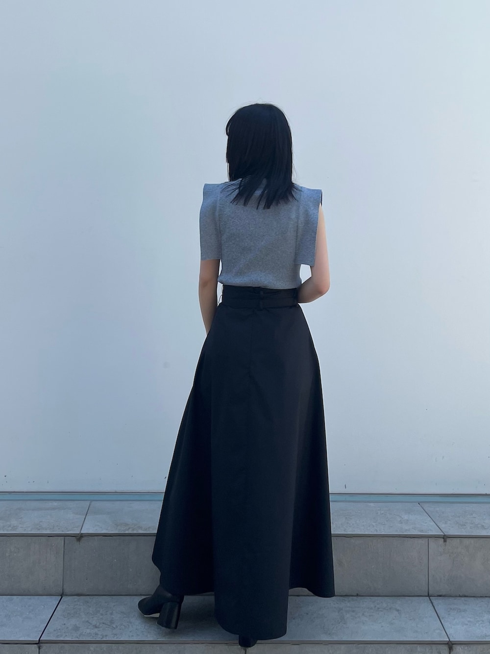 ブルー系のニット/セーター、ブラック系のスカート、ベージュ系のハンドバッグを着用したレディースの春コーディネートの3枚目の写真