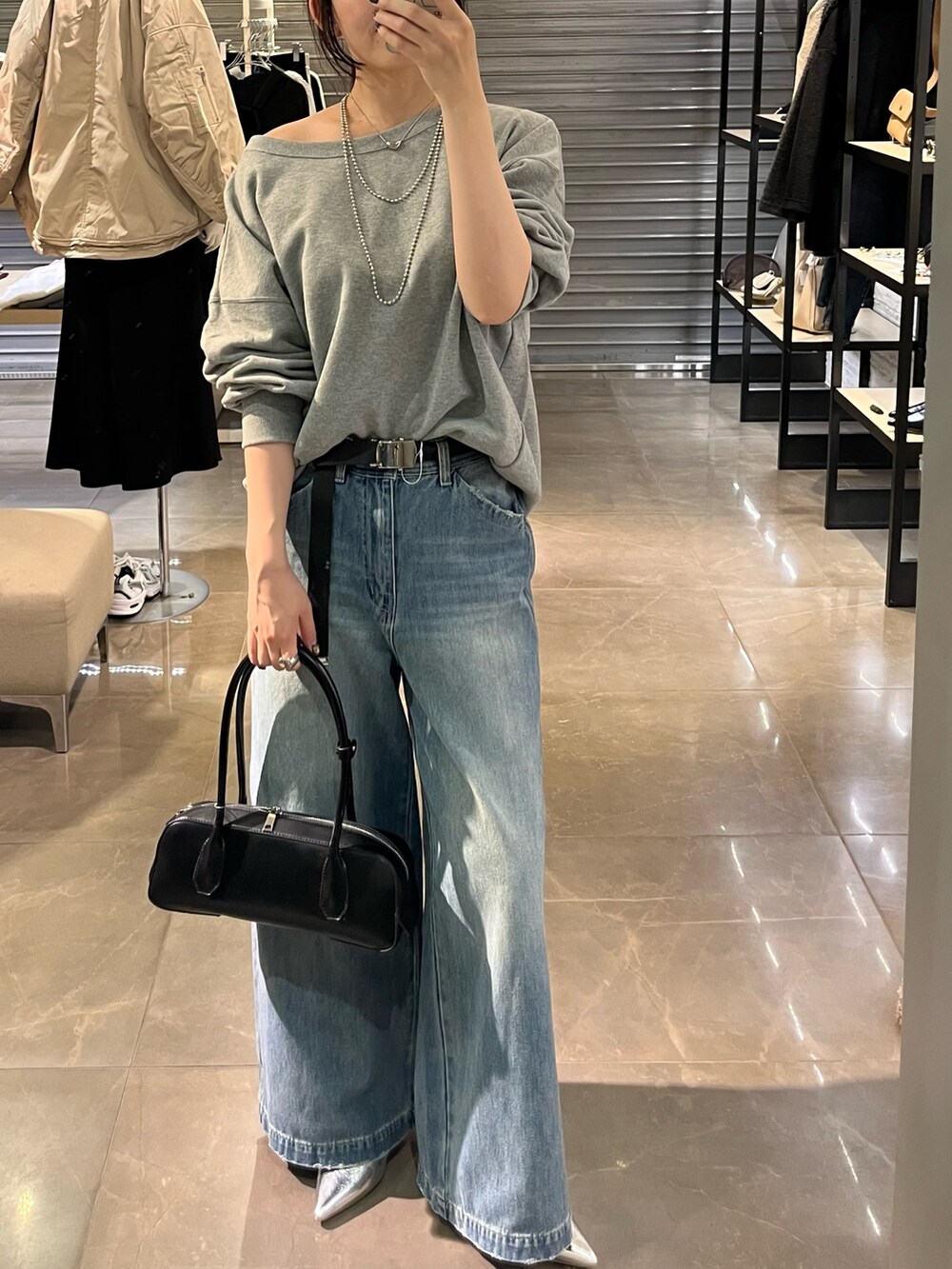 シルバー系のパンプス、ホワイト系のショルダーバッグ、ブルー系のデニムパンツを着用したレディースの秋コーディネートの2枚目の写真