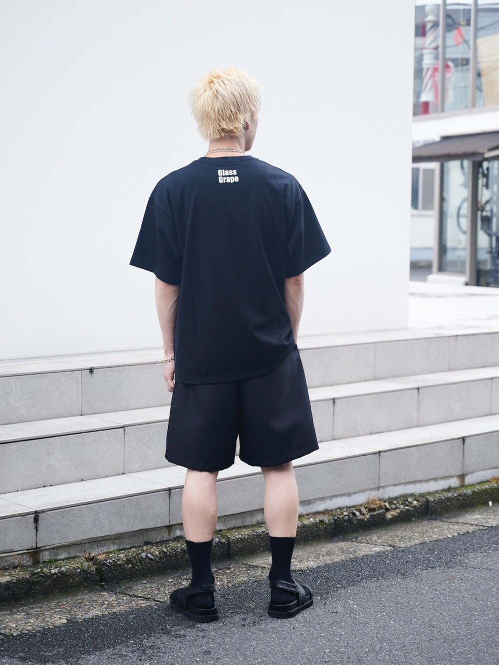 ホワイト系のTシャツ/カットソー、ブラック系のスラックス、ブラック系のサンダルを着用したメンズの夏コーディネートの3枚目の写真