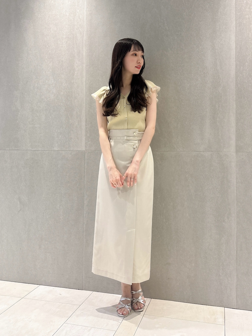 ベージュ系のスカート、イエロー系のニット/セーター、シルバー系のパンプスを着用したレディースの春コーディネートの2枚目の写真