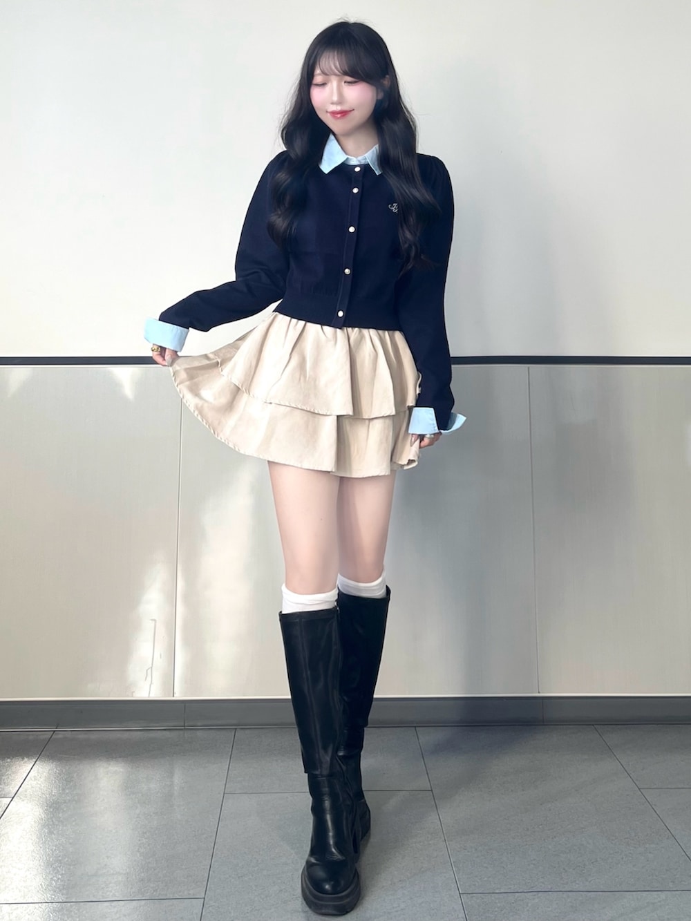 ブルー系のニット/セーター、ホワイト系のスカート、ブラック系のブーツを着用したレディースの秋コーディネートの2枚目の写真