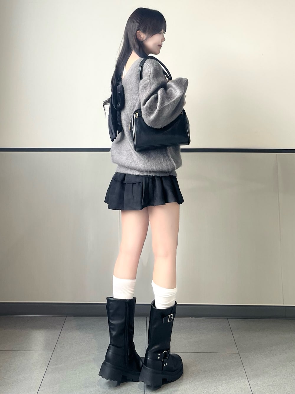 グレー系のニット/セーター、ブラック系のスカート、ブラック系のハンドバッグを着用したレディースの秋コーディネートの2枚目の写真
