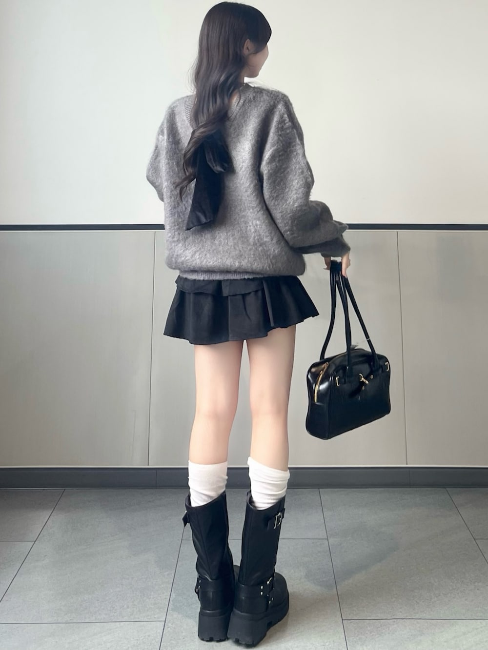 グレー系のニット/セーター、ブラック系のスカート、ブラック系のハンドバッグを着用したレディースの秋コーディネートの3枚目の写真