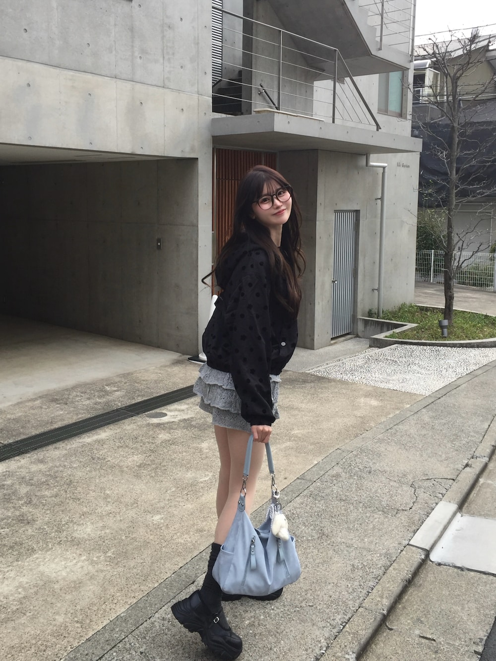 グレー系のスカート、ブラック系のナイロンジャケット、ブルー系のバッグを着用したレディースの春コーディネートの2枚目の写真