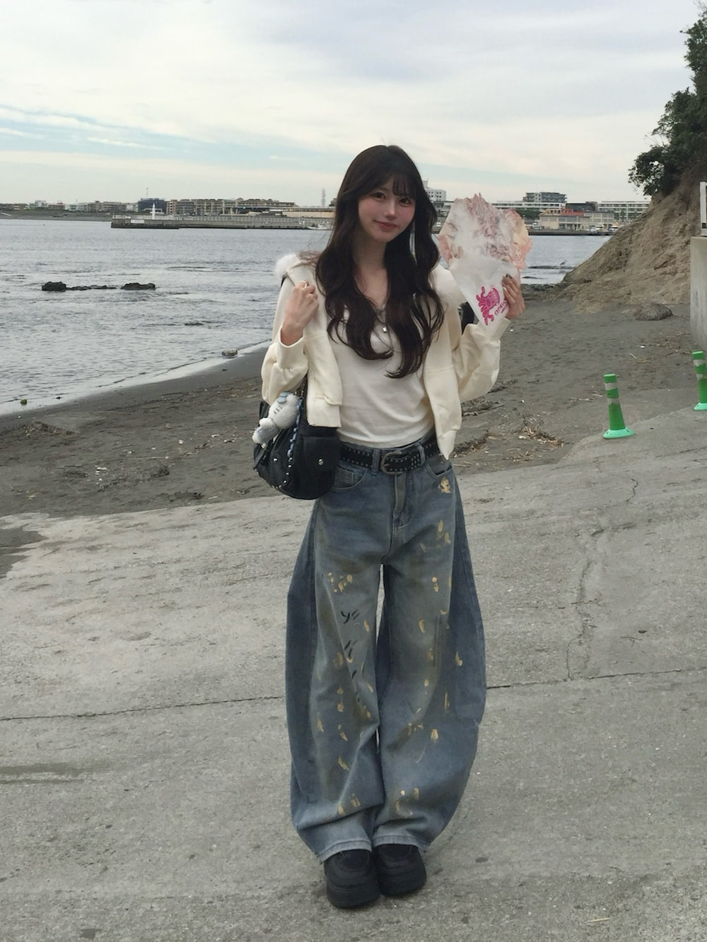 ホワイト系のパーカー、ブラック系のライダースジャケット、ブルー系のデニムパンツを着用したレディースの秋コーディネートの2枚目の写真