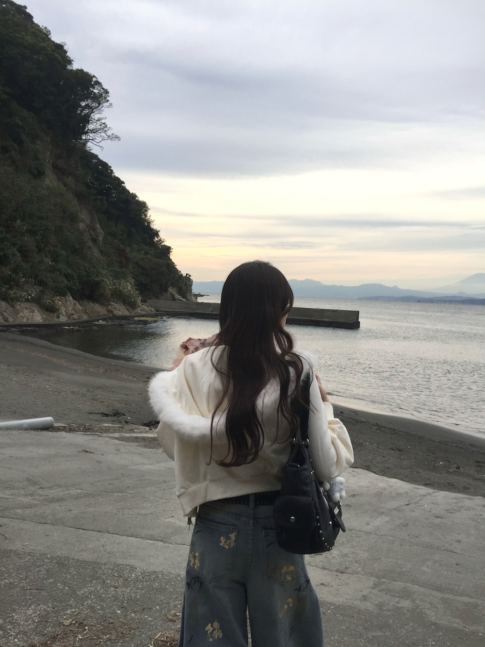 ホワイト系のパーカー、ブラック系のライダースジャケット、ブルー系のデニムパンツを着用したレディースの秋コーディネートの3枚目の写真