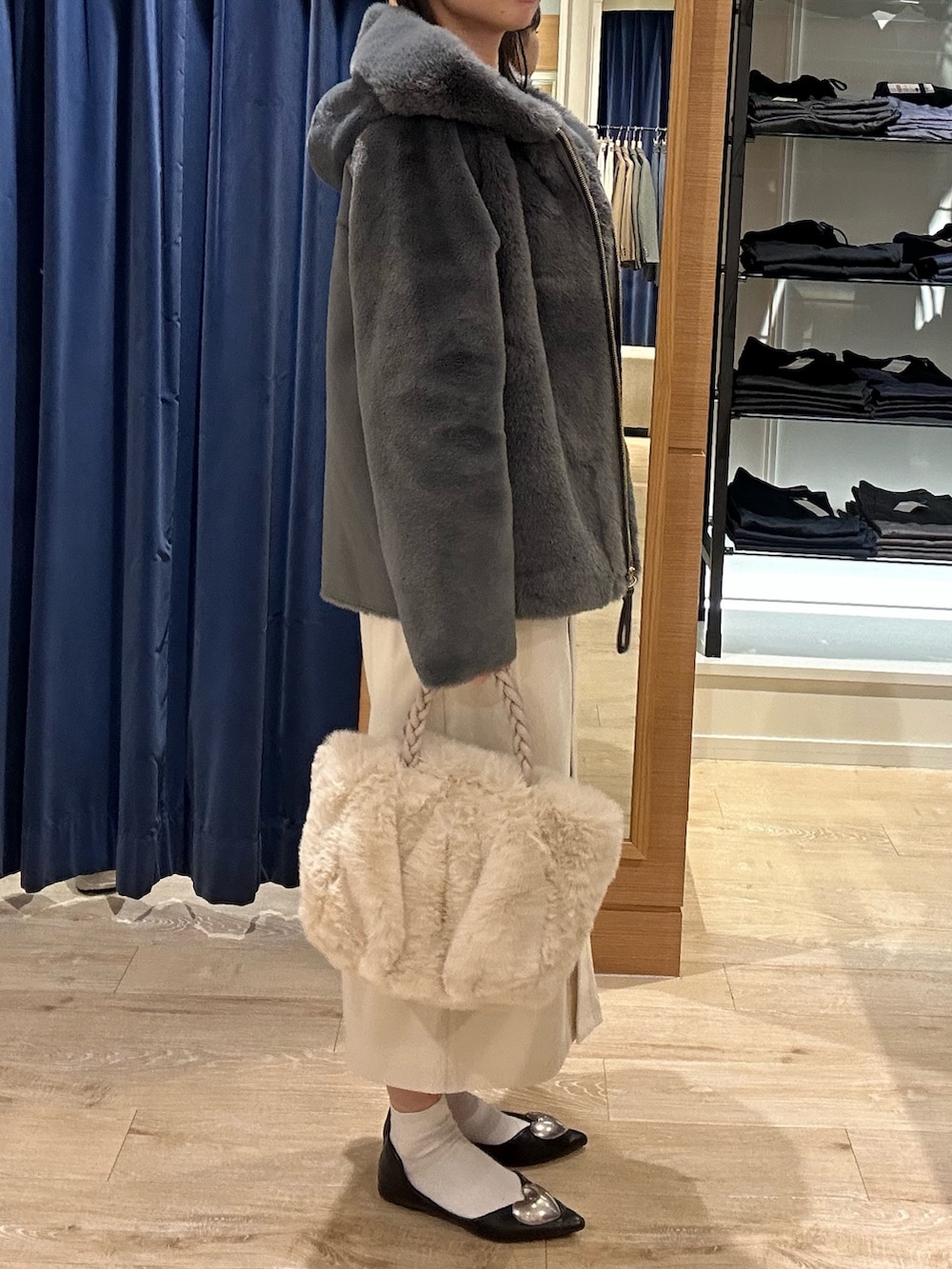 ブルー系のニット/セーター、グレー系のムートンコート、ホワイト系のトートバッグを着用したレディースの冬コーディネートの2枚目の写真