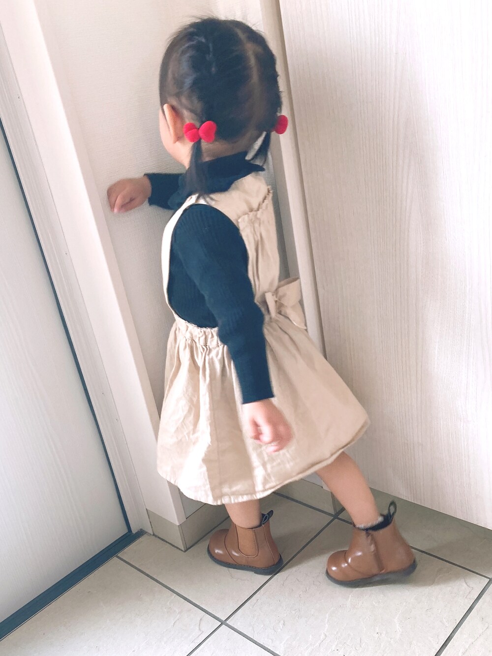 ブラック系のニット/セーター、ブラウン系のブーツ、ベージュ系のジャンパースカートを着用したキッズの秋コーディネートの2枚目の写真