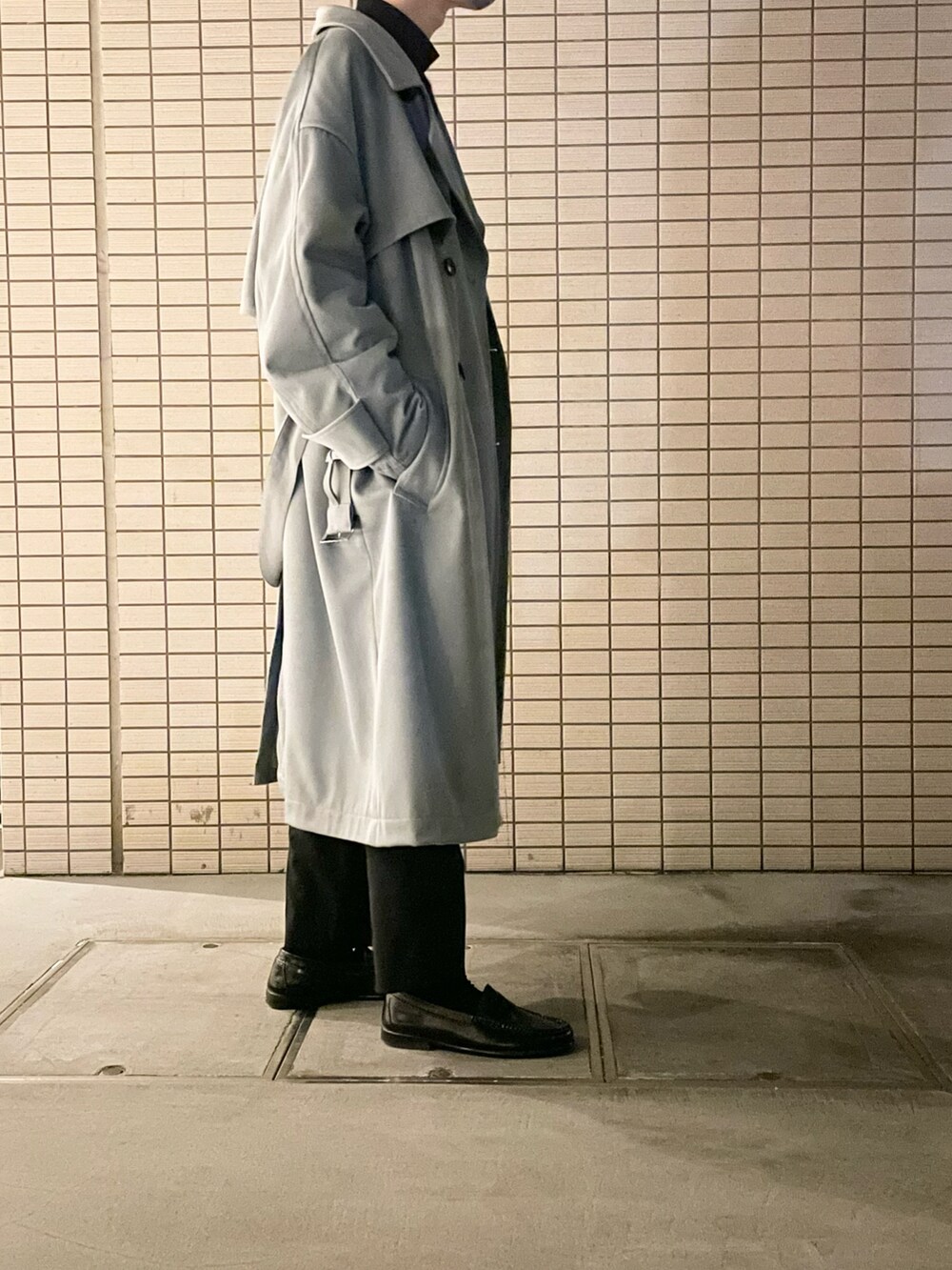 グレー系のトレンチコート、ブラック系のニット/セーター、ブラック系のスラックスを着用したメンズの冬コーディネートの3枚目の写真