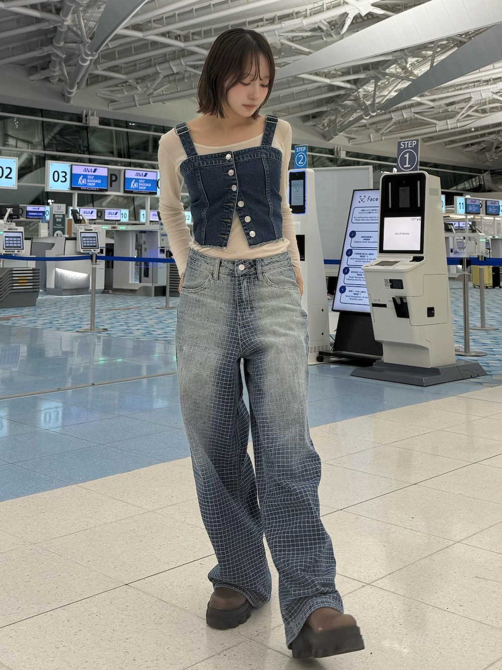 ブラウン系のブーツ、ブルー系のベスト、ブルー系のデニムパンツを着用したレディースの春コーディネートの2枚目の写真