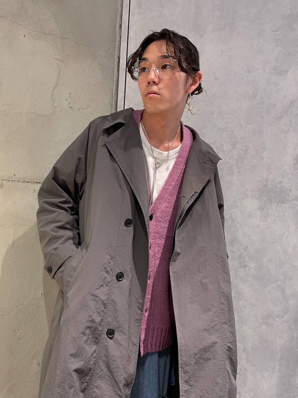 グレー系のステンカラーコート、ピンク系のカーディガン/ボレロ、ブルー系のデニムパンツを着用したメンズの秋コーディネートの3枚目の写真