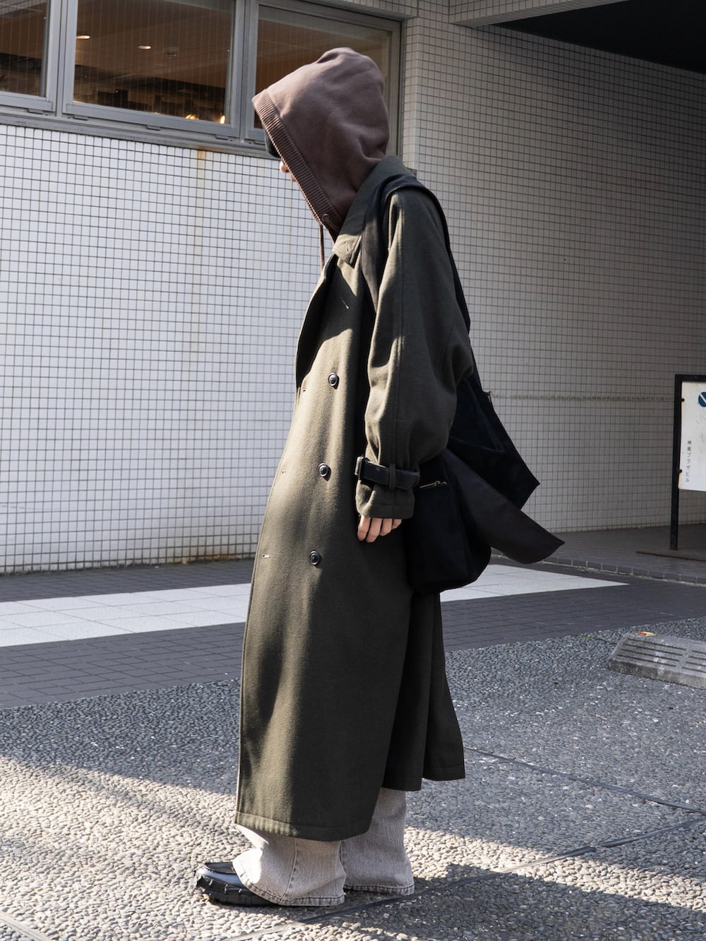 グリーン系のステンカラーコート、グレー系のデニムパンツ、ブラック系のローファーを着用したメンズの秋コーディネートの2枚目の写真