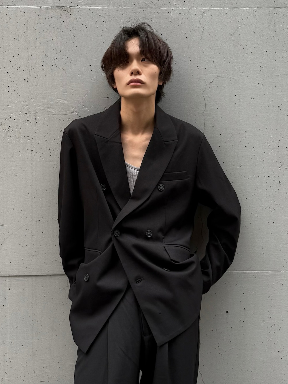 グレー系のタンクトップ、ブラック系のテーラードジャケット、ブラック系のスラックスを着用したメンズの秋コーディネートの2枚目の写真