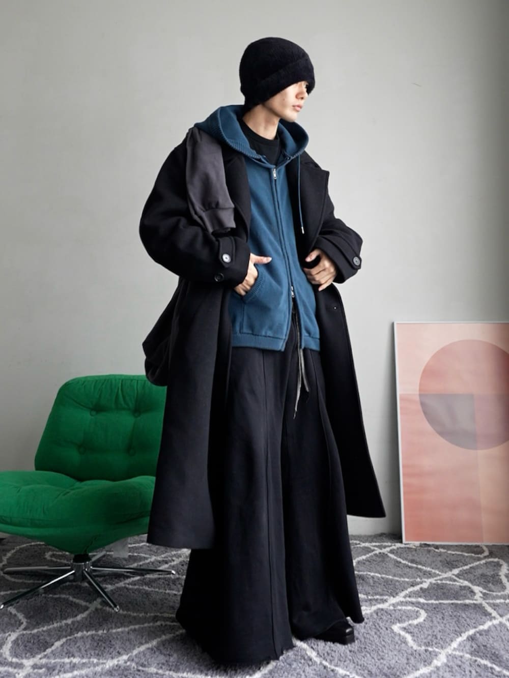 ブラック系のチェスターコート、ブルー系のパーカー、ブラック系のスウェットパンツを着用したメンズの秋コーディネートの2枚目の写真