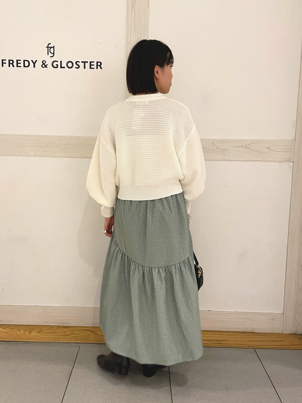 ホワイト系のカーディガン/ボレロ、ホワイト系のショルダーバッグ、グリーン系のスカートを着用したレディースの春コーディネートの2枚目の写真