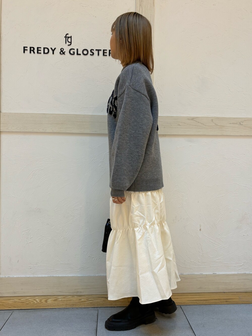 ブラック系のショルダーバッグ、イエロー系のスカート、ブルー系のニット/セーターを着用したレディースの冬コーディネートの2枚目の写真