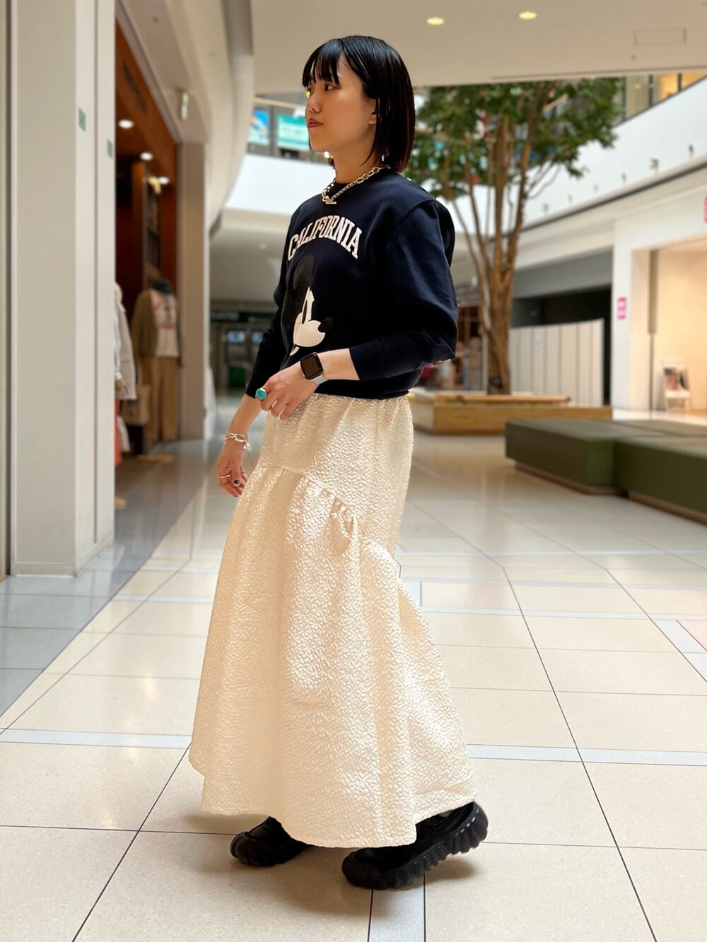 グレー系のスウェット、ホワイト系のスカート、ブラック系のスニーカーを着用したレディースの春コーディネートの2枚目の写真