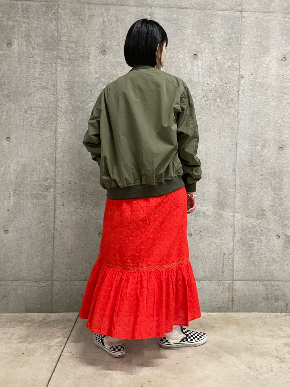 グレー系のTシャツ/カットソー、レッド系のスカート、グリーン系のブルゾンを着用したレディースの春コーディネートの3枚目の写真