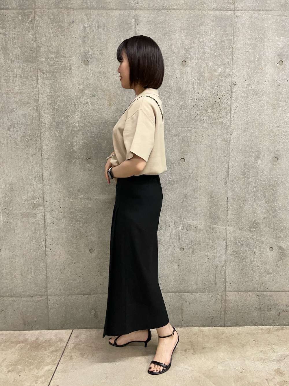 ブラック系のスカート、ブラック系のショルダーバッグ、ベージュ系のポロシャツを着用したレディースの春コーディネートの2枚目の写真