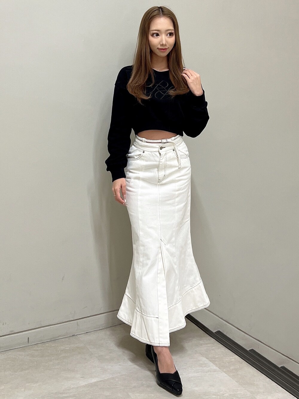 ブラック系のスウェット、ホワイト系のデニムスカート、ブラック系のパンプスを着用したレディースの冬コーディネートの2枚目の写真