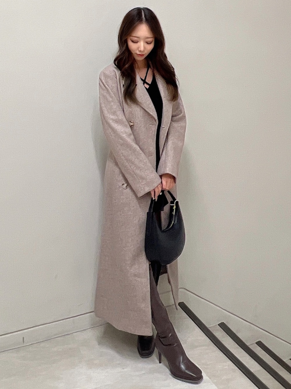 ブラウン系のチェスターコート、ブラウン系のブーツ、ブラック系のニット/セーターを着用したレディースの冬コーディネートの2枚目の写真