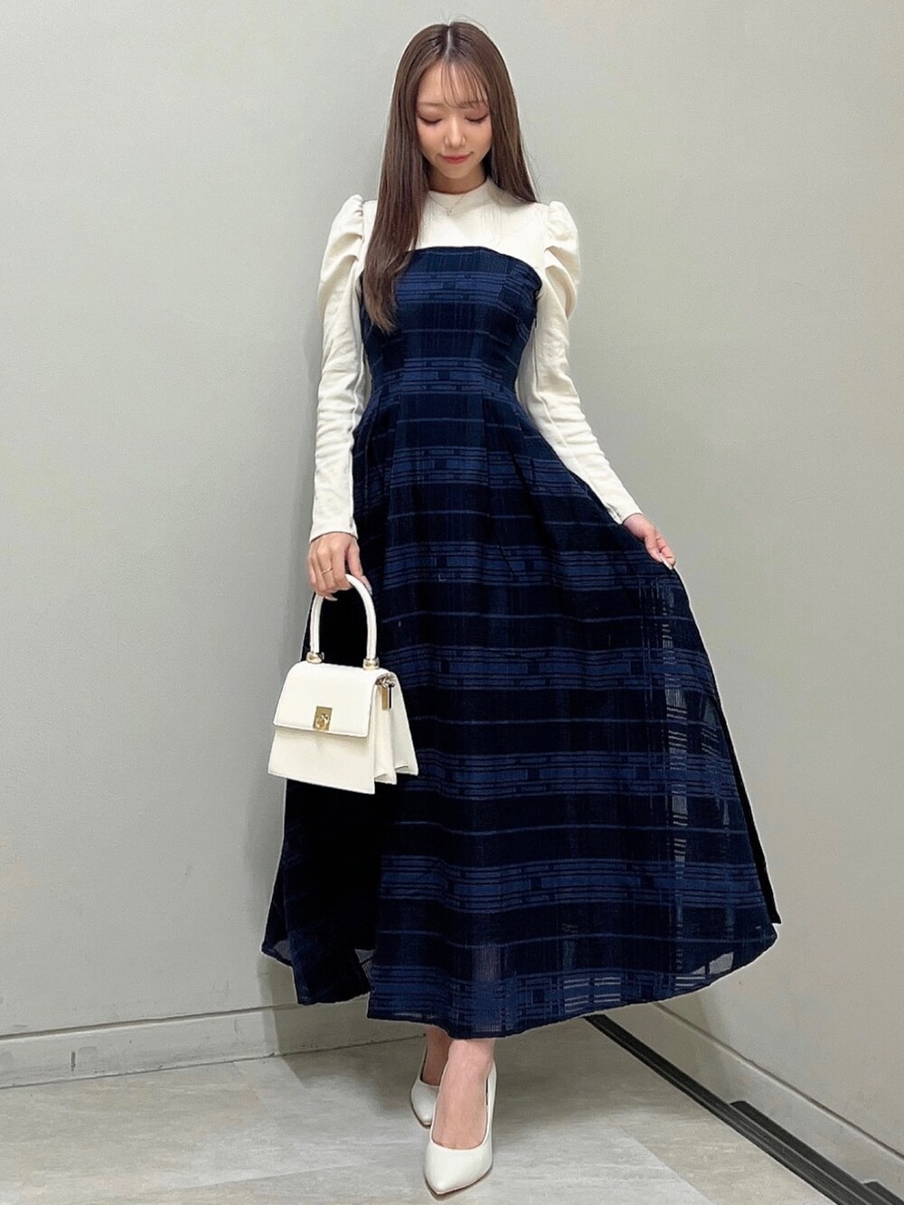 ホワイト系のパンプス、ブルー系のワンピース、ホワイト系のハンドバッグを着用したレディースの冬コーディネートの2枚目の写真