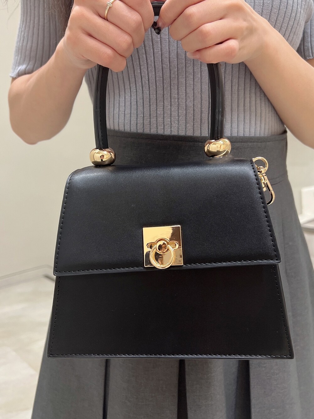 ブルー系のニット/セーター、グレー系のスカート、ブラック系のハンドバッグを着用したレディースの春コーディネートの7枚目の写真