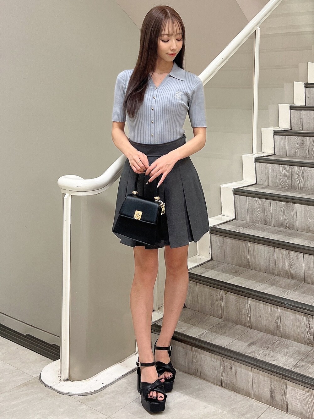 ブルー系のニット/セーター、グレー系のスカート、ブラック系のハンドバッグを着用したレディースの春コーディネートの2枚目の写真