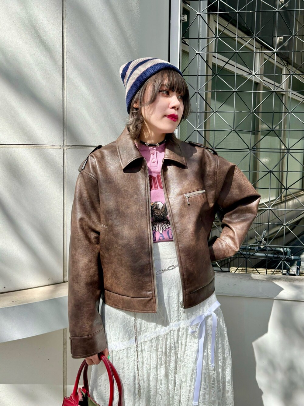 レッド系のハンドバッグ、レッド系のパンプス、ブラウン系のブルゾンを着用したレディースの夏コーディネートの4枚目の写真