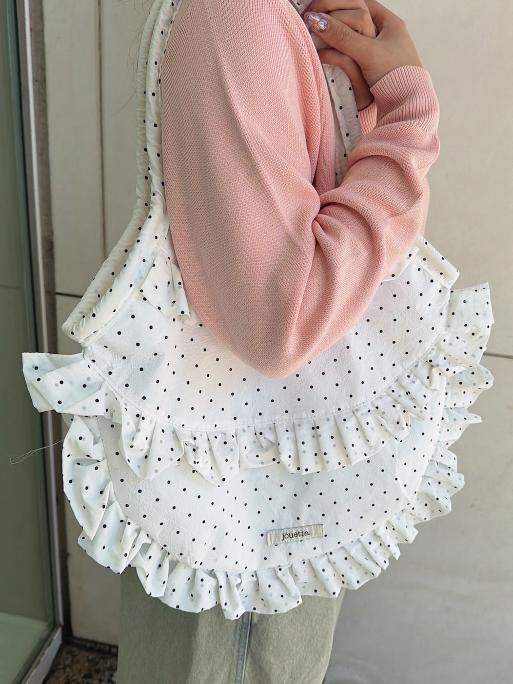 ピンク系のニット/セーター、ホワイト系のトートバッグ、ブルー系のデニムパンツを着用したレディースの春コーディネートの8枚目の写真